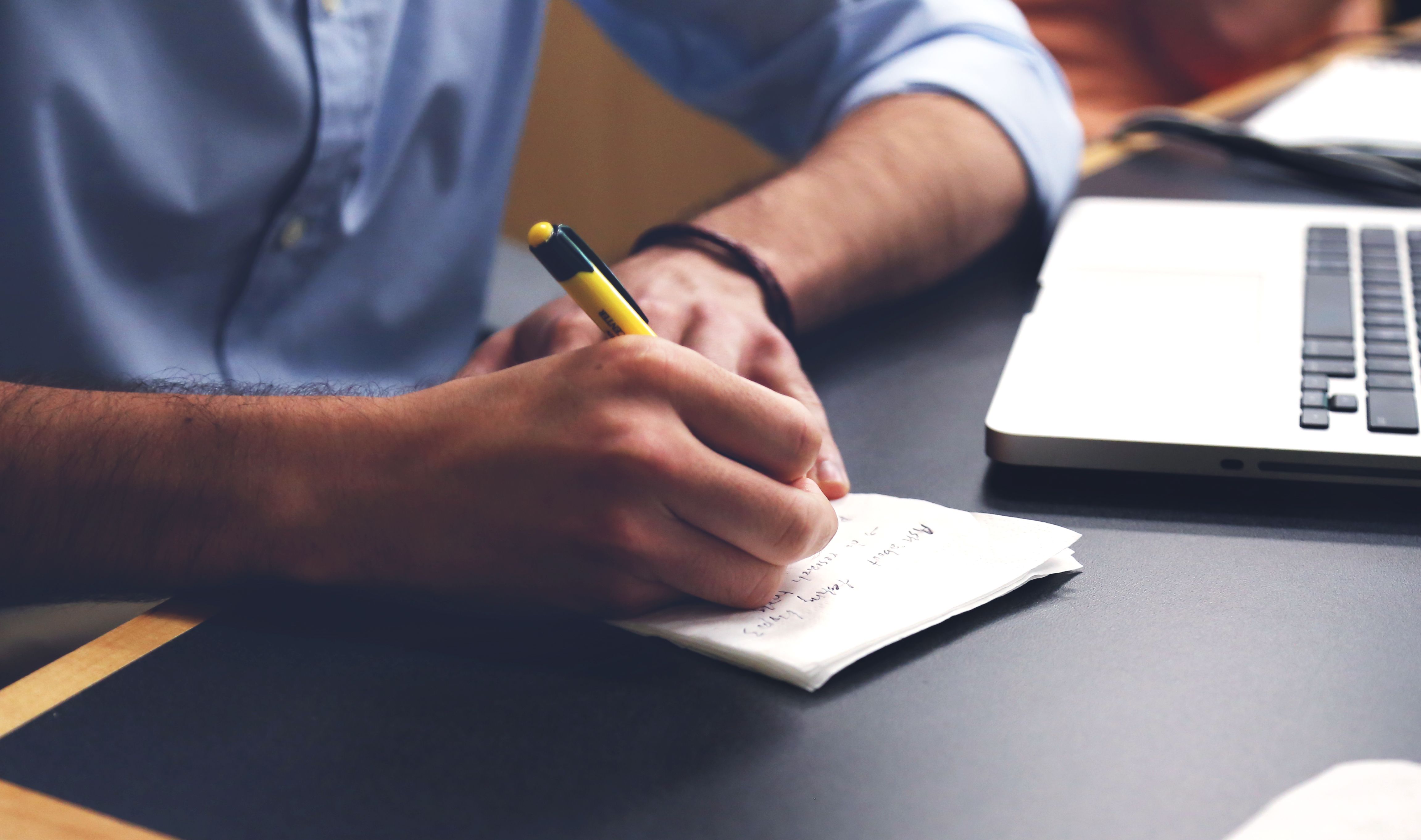 Person writing notes with a pen next to a laptop while drafting a plan for how to start a business